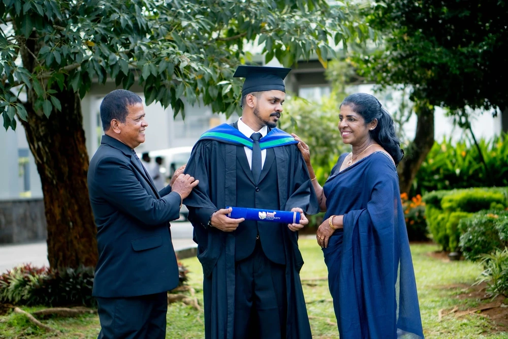 A graduate standing with his parents in a garden